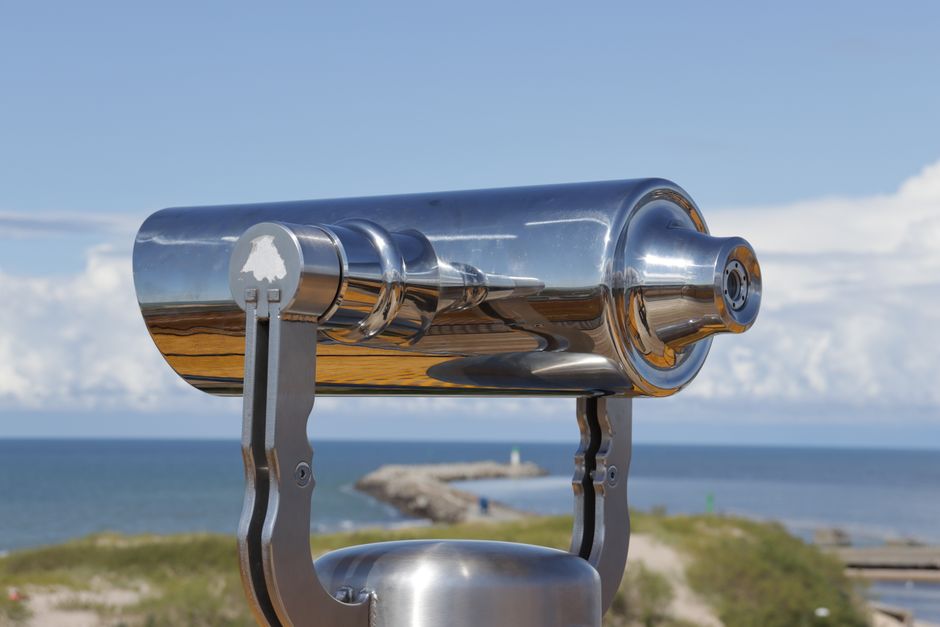A shiny metallic telescope overlooks the ocean on a clear day, offering scenic views.